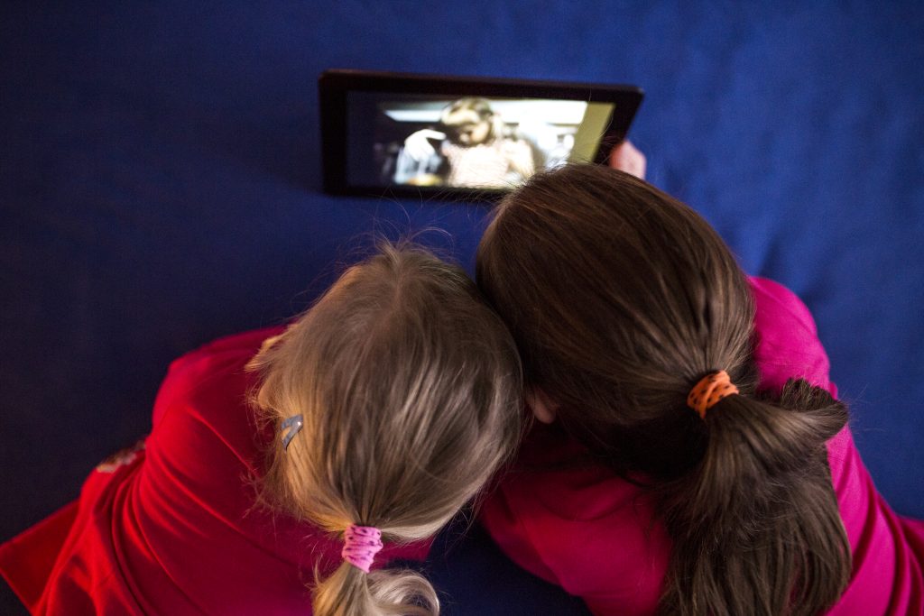 Duas crianças deitadas e assistindo programação de tablet, juntas